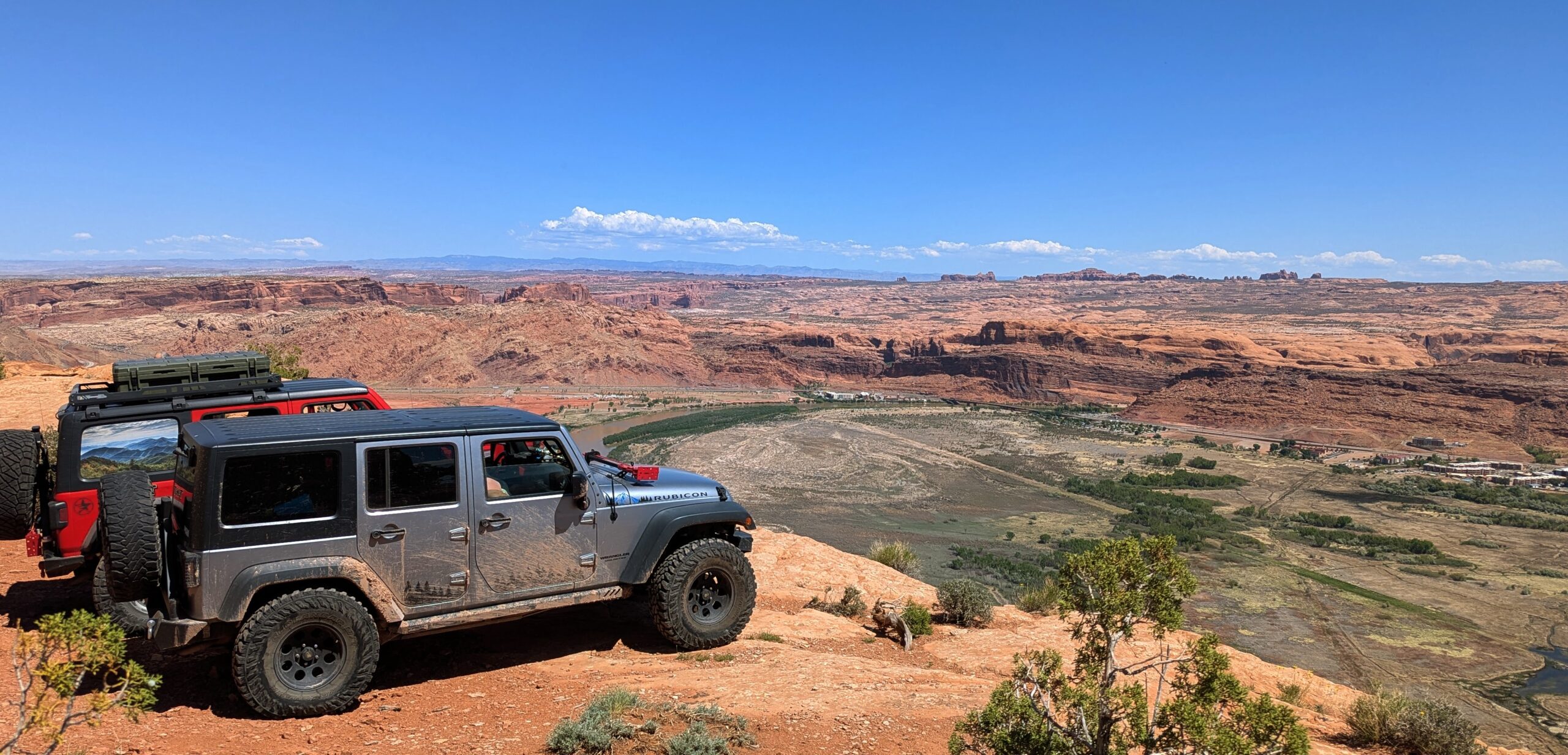 Photo of two Jeeps parked side by side overlooking the Colorado River valley and the city of Moab from Poison Spider trail.
